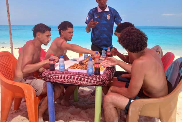 Group of young men enjoying a meal under a beach umbrella on Nakupenda Sandbank.